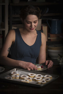 Backen zum Valentinstag, junge Frau sitzt in einer Küche, mit einem Backblech mit herzförmigen Keksen. - MINF06171