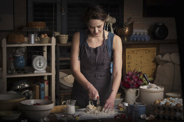 Valentine's Day baking, young woman standing in a kitchen, preparing dough for biscuits. - MINF06177