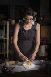 Backen zum Valentinstag, junge Frau steht in einer Küche und bereitet Teig für Kekse vor. - MINF06181