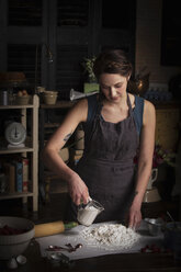 Valentine's Day baking, young woman standing in a kitchen, preparing dough for biscuits, pouring milk from a jug. - MINF06182