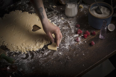 Valentine's Day baking, woman cutting out heart shaped biscuits from dough. - MINF06186