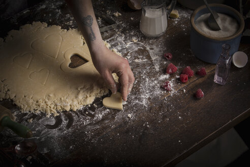 Backen zum Valentinstag, Frau sticht herzförmige Kekse aus dem Teig aus. - MINF06186