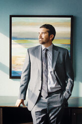 Porträt eines Mannes im Anzug, eines Geschäftsmannes, der vor einem Kunstwerk steht. - MINF06210