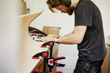 Eine Möbelwerkstatt, die maßgeschneiderte zeitgenössische Möbelstücke herstellt und dabei traditionelle Fertigkeiten mit modernem Design verbindet. Ein Mann an einer Werkbank, der ein Stück gebogenes Holz mit Klammern bearbeitet. - MINF06214