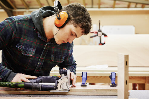 Eine Möbelwerkstatt, die maßgeschneiderte zeitgenössische Möbelstücke herstellt und dabei traditionelle Fertigkeiten mit modernem Design verbindet. Ein junger Mann benutzt Werkzeuge, um ein Stück Holz zu formen. - MINF06217