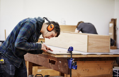 Eine Möbelwerkstatt, die zeitgenössische Möbelstücke nach Maß herstellt und dabei traditionelle Fertigkeiten mit modernem Design verbindet. Ein Mann markiert ein Stück Holz mit einem Bleistift. - MINF06222