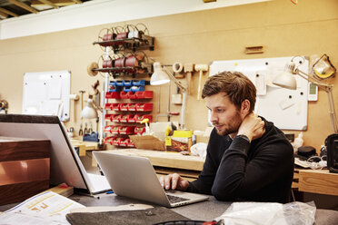 Eine Möbelwerkstatt, die maßgeschneiderte zeitgenössische Möbelstücke herstellt und dabei traditionelle Fertigkeiten mit modernem Design verbindet. Ein Mann sitzt an einem Laptop. - MINF06225