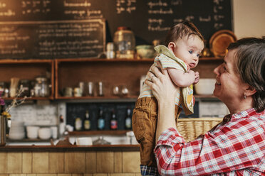 A woman holding up a young baby at a coffee shop. - MINF06236