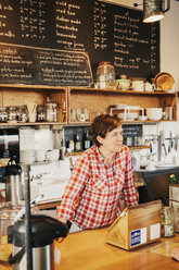 Eine Frau in einem karierten Hemd arbeitet hinter dem Tresen eines Cafés. - MINF06240