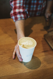 Eine Person, die eine Tasse frisch gebrühten Kaffee mit Schaum und Farnmuster auf die Oberfläche eines Holztisches stellt. - MINF06244