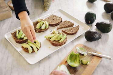 A woman preparing open sandwiches with brown bread and avocado. - MINF06253