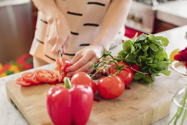 A person at a kitchen counter preparing salad, chopping fresh tomatoes. - MINF06254