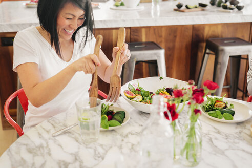 Eine Frau benutzt ein Salatbesteck, um ihren Teller mit frischen Salatblättern zu füllen. - MINF06260
