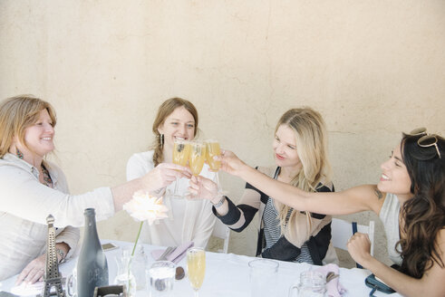 Vier lächelnde Frauen sitzen an einem Tisch, halten Gläser mit Champagner in der Hand und stoßen an. - MINF06277