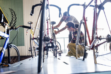 Ein Mann arbeitet in einer Fahrradwerkstatt und überprüft ein Fahrrad mit einem Kunden. - MINF06285