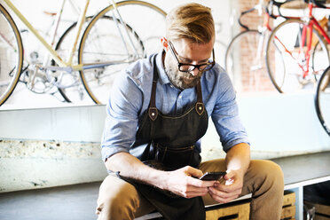 Ein Mann, der in einer Fahrradwerkstatt arbeitet, überprüft sein Telefon auf Nachrichten. Kaffeepause. - MINF06288