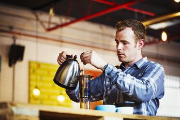 Spezialisiertes Café: Ein Mann gießt heißes Wasser in eine Kaffeemaschine. - MINF06308