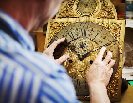 Ein Uhrmacher bewegt die Zeiger einer antiken Uhr, repariert die Uhr und stellt sie neu ein. - MINF06315