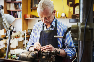 Ein Uhrmacher und Reparateur bei der Arbeit an den Kleinteilen einer Uhr an einer Werkbank. - MINF06321