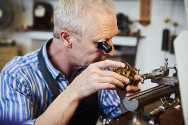 Ein Uhrmacher, der eine Brille benutzt, um an kleinen Mechanismen in einer Uhr zu arbeiten. - MINF06323