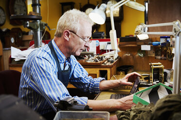 Ein Uhrenreparateur, ein Handwerker in seiner Werkstatt mit einem Laptop. - MINF06324