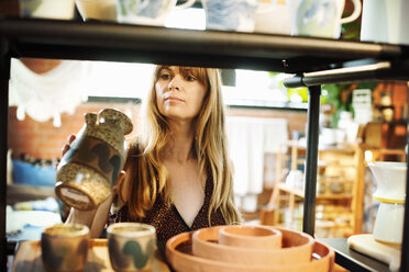 Eine Frau steht in einem Geschäft und hält eine kleine Keramikvase. - MINF06358