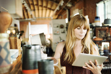 Frau in einem Geschäft, die ein digitales Tablet und eine Keramikkanne in der Hand hält. - MINF06362