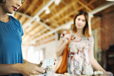 Zwei junge Frauen in einem Geschäft, die ein Kreditkartenlesegerät benutzen. - MINF06389