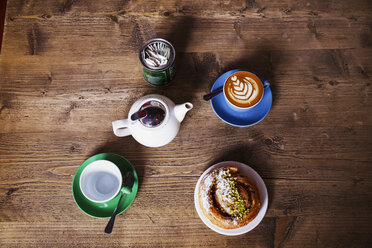 Spezialisiertes Café. Blick auf einen Tisch mit einer Tasse Kaffee, einer Teekanne und einer Teetasse sowie einem Gebäck auf einem Teller. - MINF06408