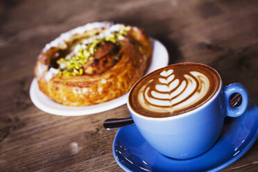 Eine Tasse Kaffee mit einem Farnblattmuster auf dem Schaum und ein Croissant auf einem Teller. - MINF06409