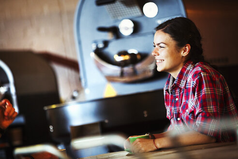 Spezialisiertes Café: Eine Frau sitzt am Tresen neben einer Röstmaschine. - MINF06420