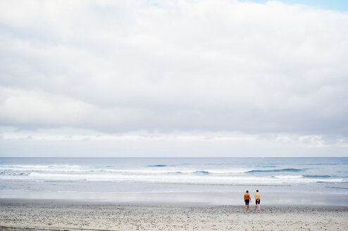 Zwei Männer stehen an einem Sandstrand am Meer. - MINF06455