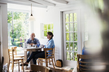 Zwei Personen sitzen an einem Tisch in einem Café am Fenster, der Vordergrund ist unscharf. - MINF06469