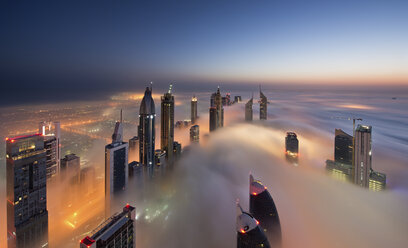Blick auf beleuchtete Wolkenkratzer über den Wolken in Dubai, Vereinigte Arabische Emirate, in der Abenddämmerung. - MINF06513