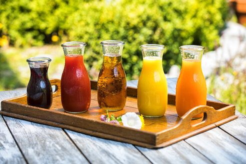 Glasflaschen mit verschiedenen Fruchtsäften auf Holztablett - MAEF12685