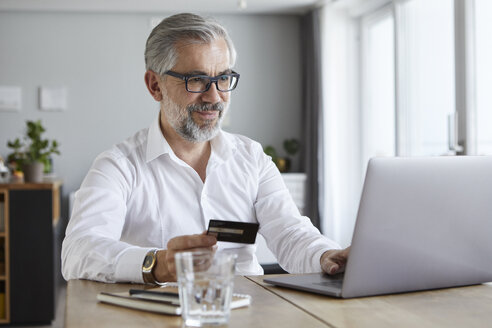 Portrait of content mature man paying online with credit card at home - RBF06468