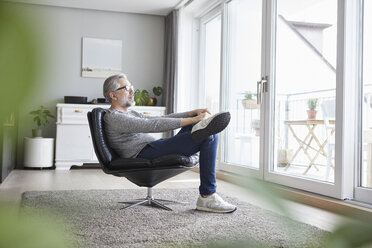 Älterer Mann entspannt sich auf einem Ledersessel in seinem Wohnzimmer und schaut aus dem Fenster - RBF06473