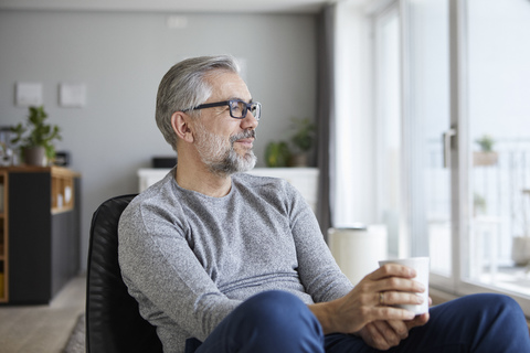 Zufriedener reifer Mann entspannt sich mit einer Tasse Kaffee zu Hause, lizenzfreies Stockfoto