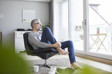 Älterer Mann entspannt sich auf einem Ledersessel in seinem Wohnzimmer und schaut aus dem Fenster - RBF06480