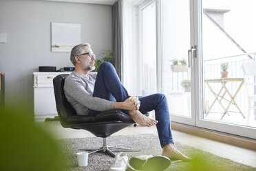 Mature man relaxing on leather chair in his living room looking out of window - RBF06480