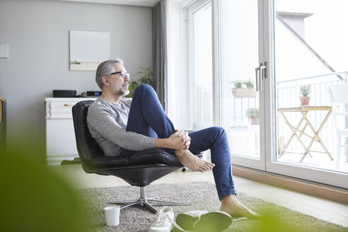 Älterer Mann entspannt sich auf einem Ledersessel in seinem Wohnzimmer und schaut aus dem Fenster - RBF06480