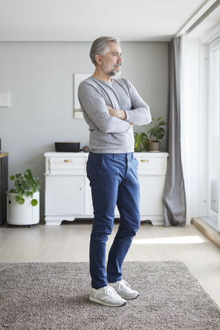 Älterer Mann steht in seinem Wohnzimmer und schaut aus dem Fenster, lizenzfreies Stockfoto