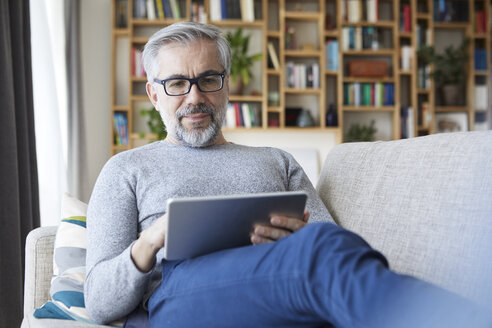 Porträt eines reifen Mannes, der auf der Couch in seinem Wohnzimmer sitzt und ein Tablet benutzt - RBF06488