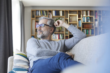 Mature man relaxing on couch at home looking out of window - RBF06489