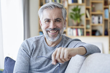 Portrait of smiling mature man sitting on couch at home - RBF06493