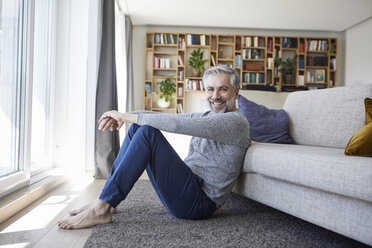 Portrait of happy mature man sitting on floor of his living room - RBF06494