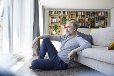 Älterer Mann sitzt auf dem Boden seines Wohnzimmers und schaut aus dem Fenster - RBF06495