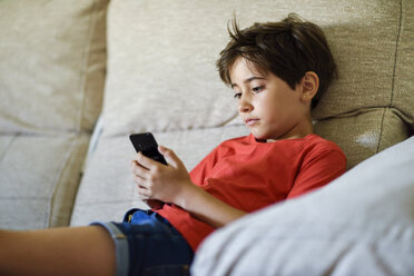 Porträt eines traurigen kleinen Mädchens auf der Couch zu Hause, das auf sein Handy schaut - JSMF00386