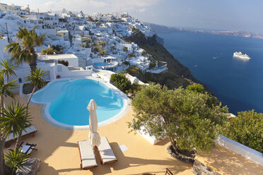 Blick von oben auf traditionelle weiß getünchte Häuser und einen Swimmingpool auf einer griechischen Insel, in der Ferne ein Schiff im Mittelmeer. - MINF06572
