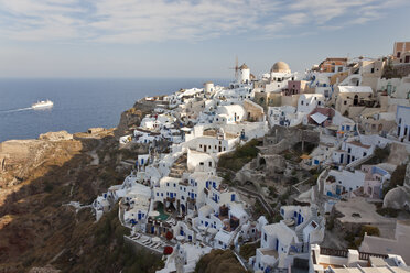 Blick von oben auf traditionelle weiß getünchte Häuser auf einer griechischen Insel, in der Ferne ein Schiff im Mittelmeer. - MINF06574